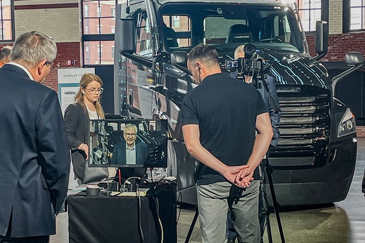 Individuals monitoring a camera shot of main speaking in front of a truck cabin